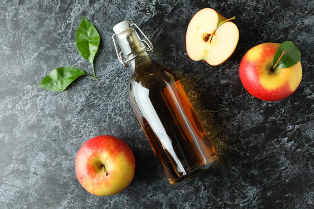 a bottle of apple cider vinegar with fresh apples on both sides