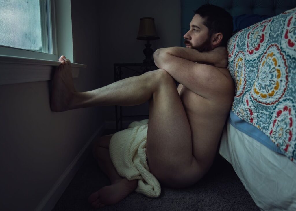 a man sitting on the bed side after masturbating and is naked