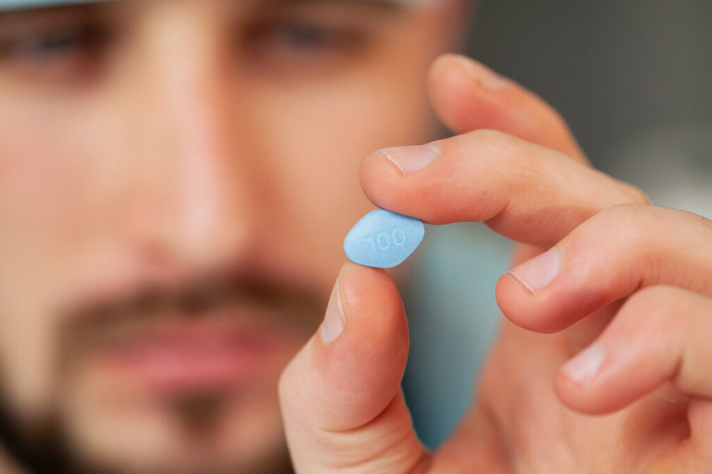 a man holds a pill of viagra using his hand while staring at it